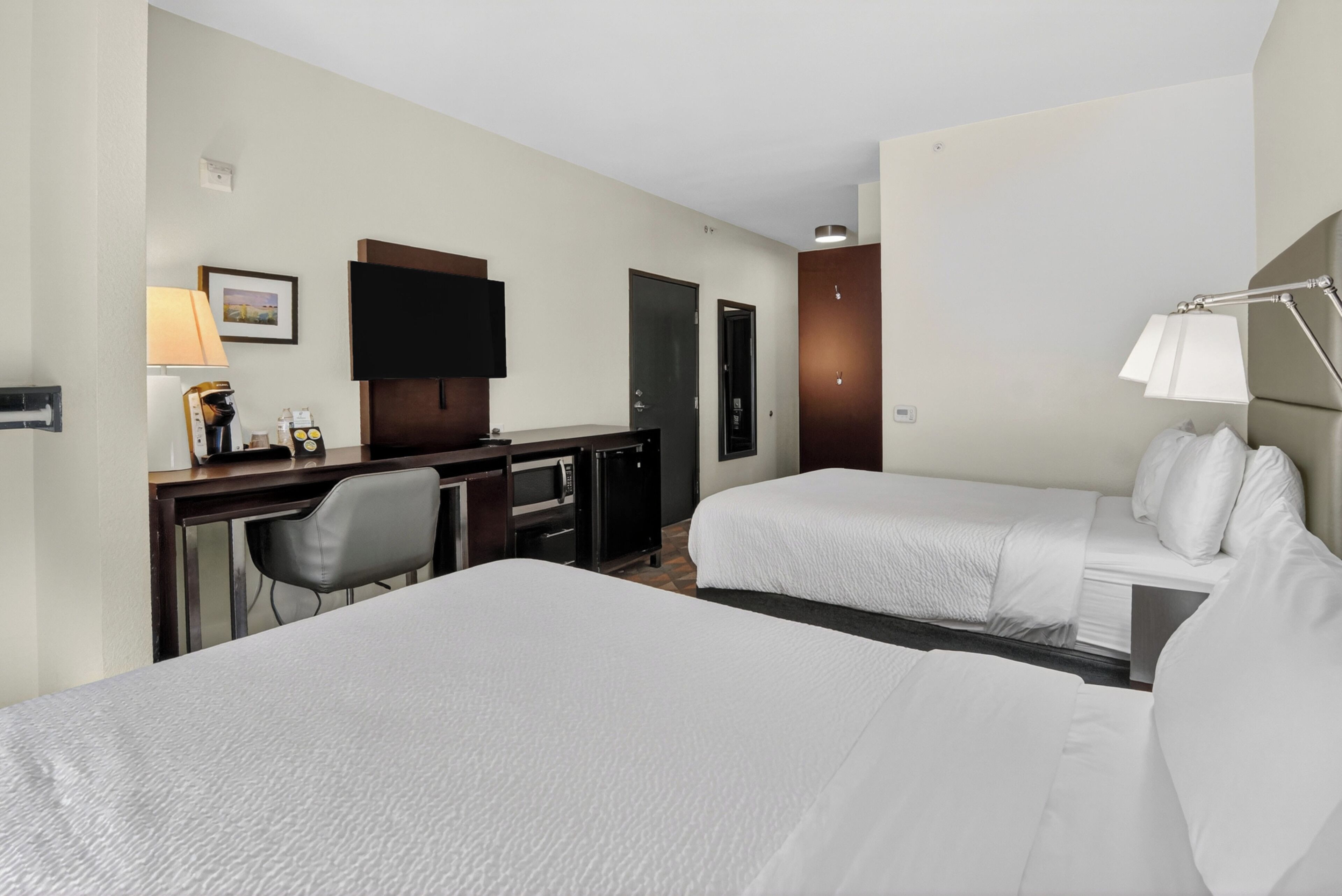 Habitación de hotel con dos camas, un escritorio, un televisor y una silla.