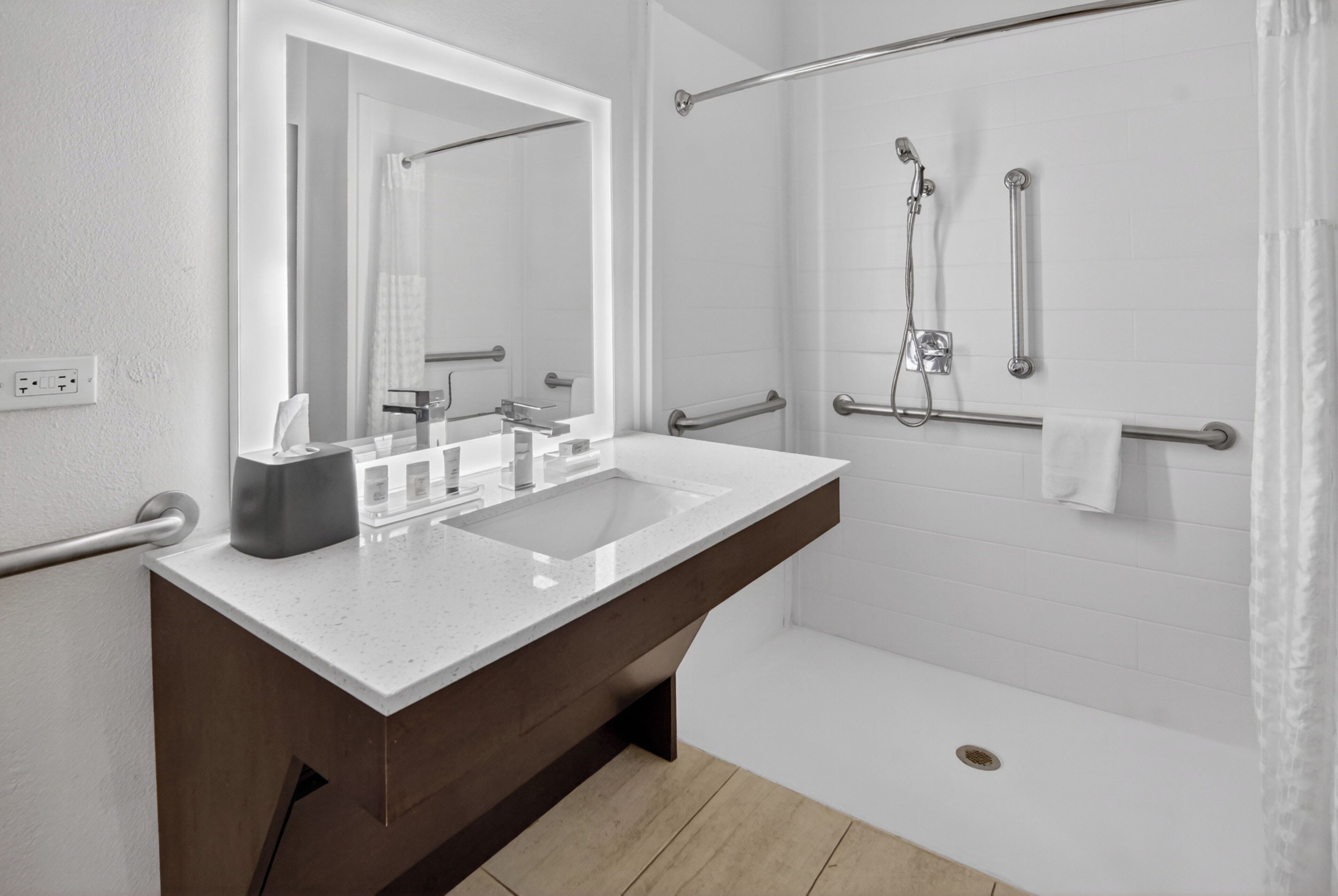 Une salle de bain moderne avec un grand miroir, un lavabo double, une douche équipée de barres d’appui et un porte-serviettes.