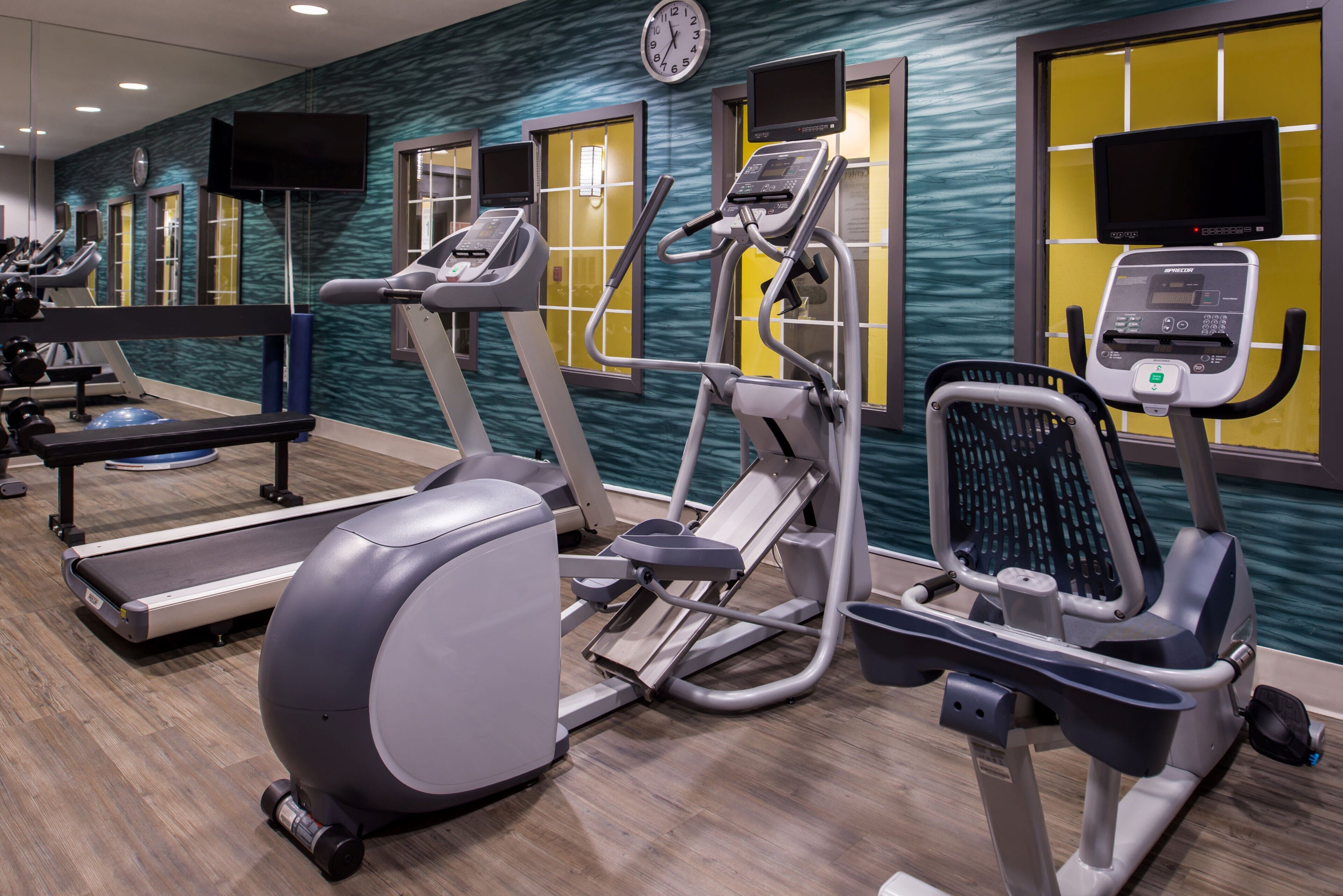 A gym with various exercise equipment, including treadmills, elliptical machines, and stationary bikes.