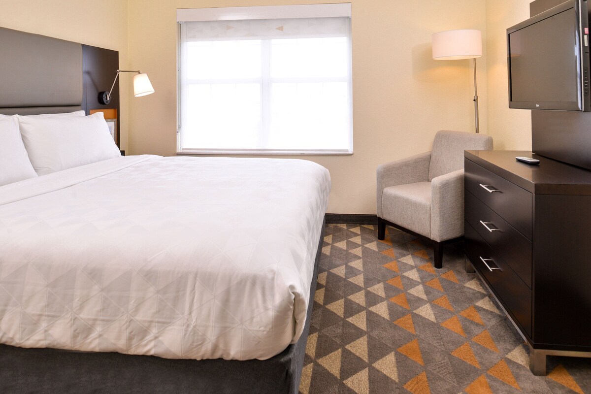 Une chambre d’hôtel avec un lit, une chaise, un bureau avec une télévision et une fenêtre.
