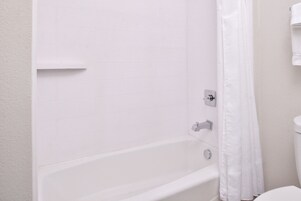 Uma banheira branca com cortina de chuveiro, um porta-toalhas e um dispensador de toalhas fixado na parede em um banheiro.
