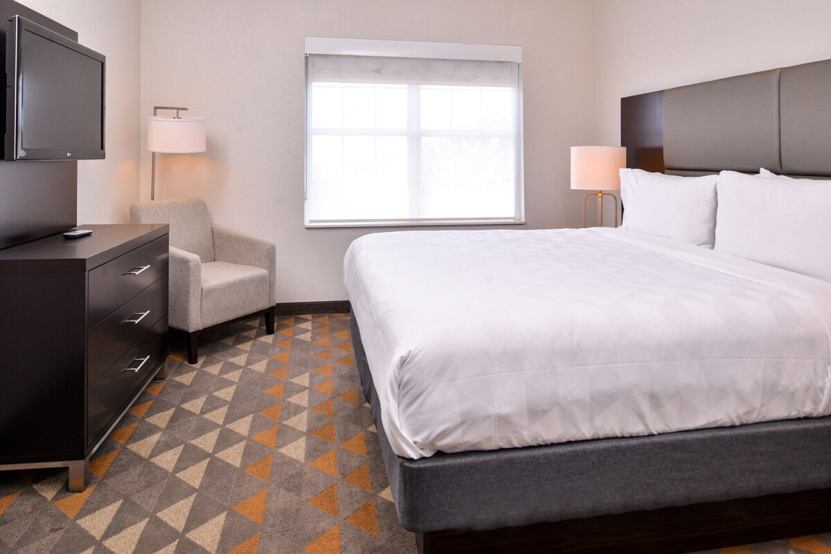 Une chambre d’hôtel avec un lit, une télévision, une chaise, une lampe et une fenêtre.