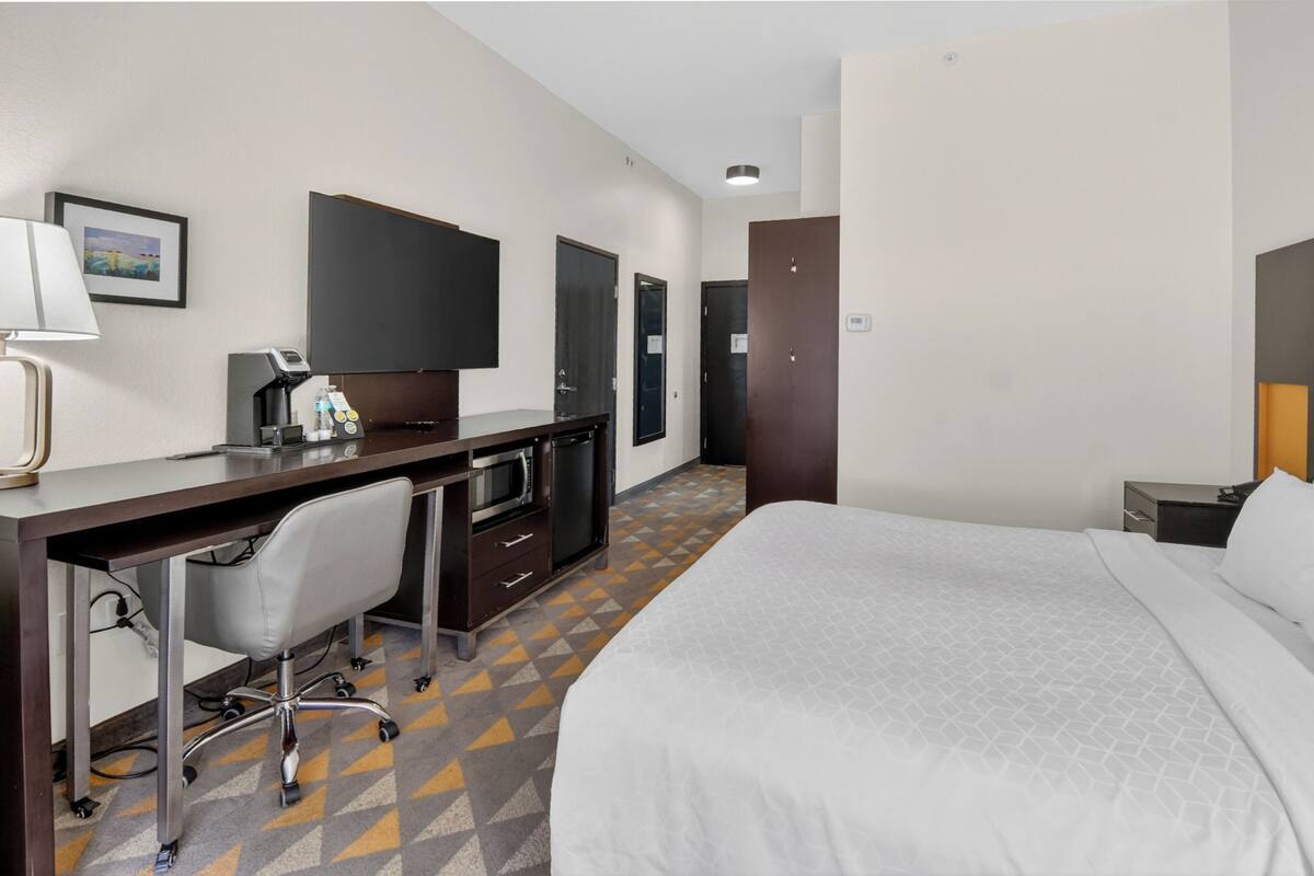 A hotel room with a bed, desk, chair, and a TV.