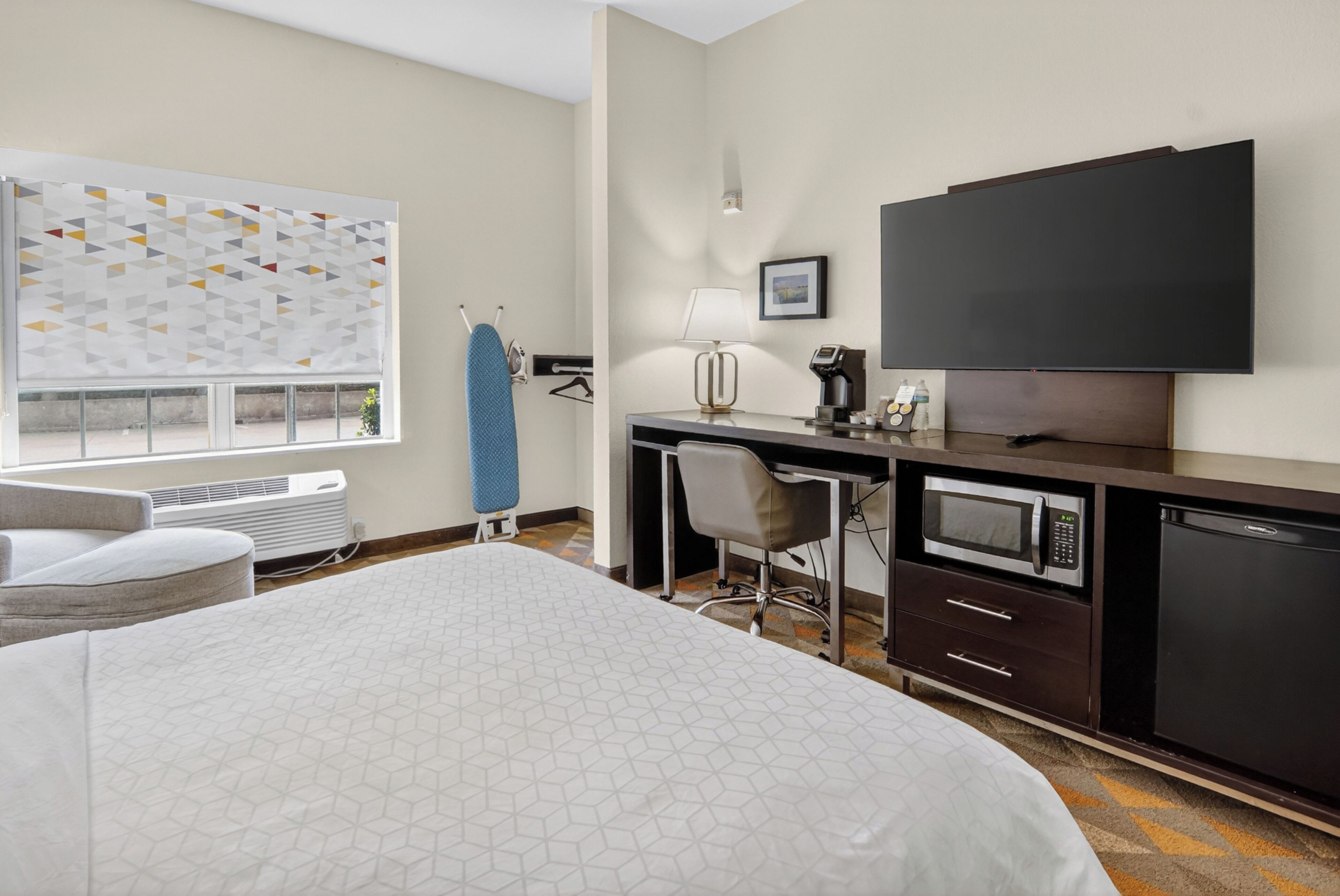 A modern hotel room with a large bed, a desk with a computer, a flat-screen TV, and a microwave.