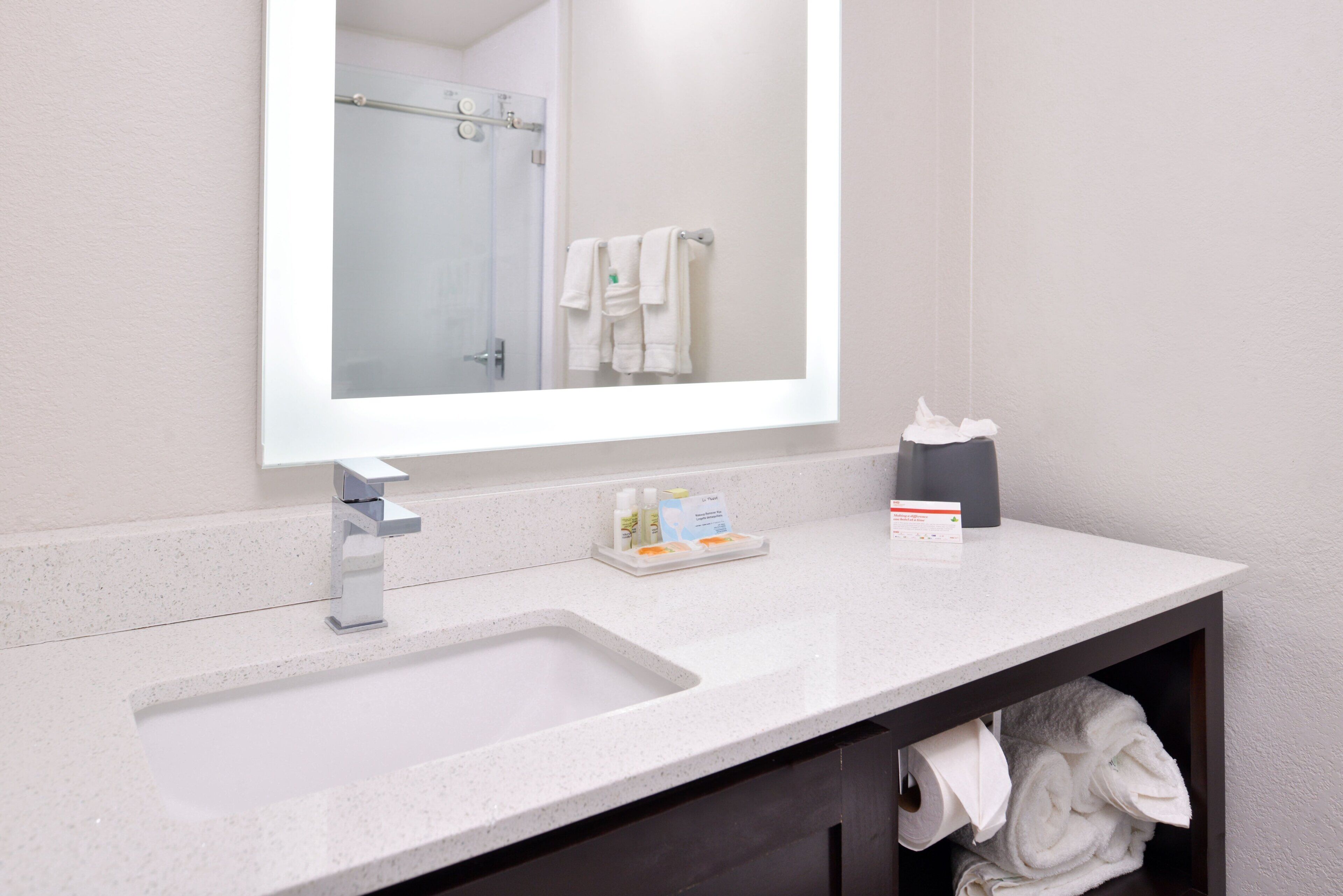 A bathroom with a sink, mirror, towel rack, and a shelf with toiletries.
