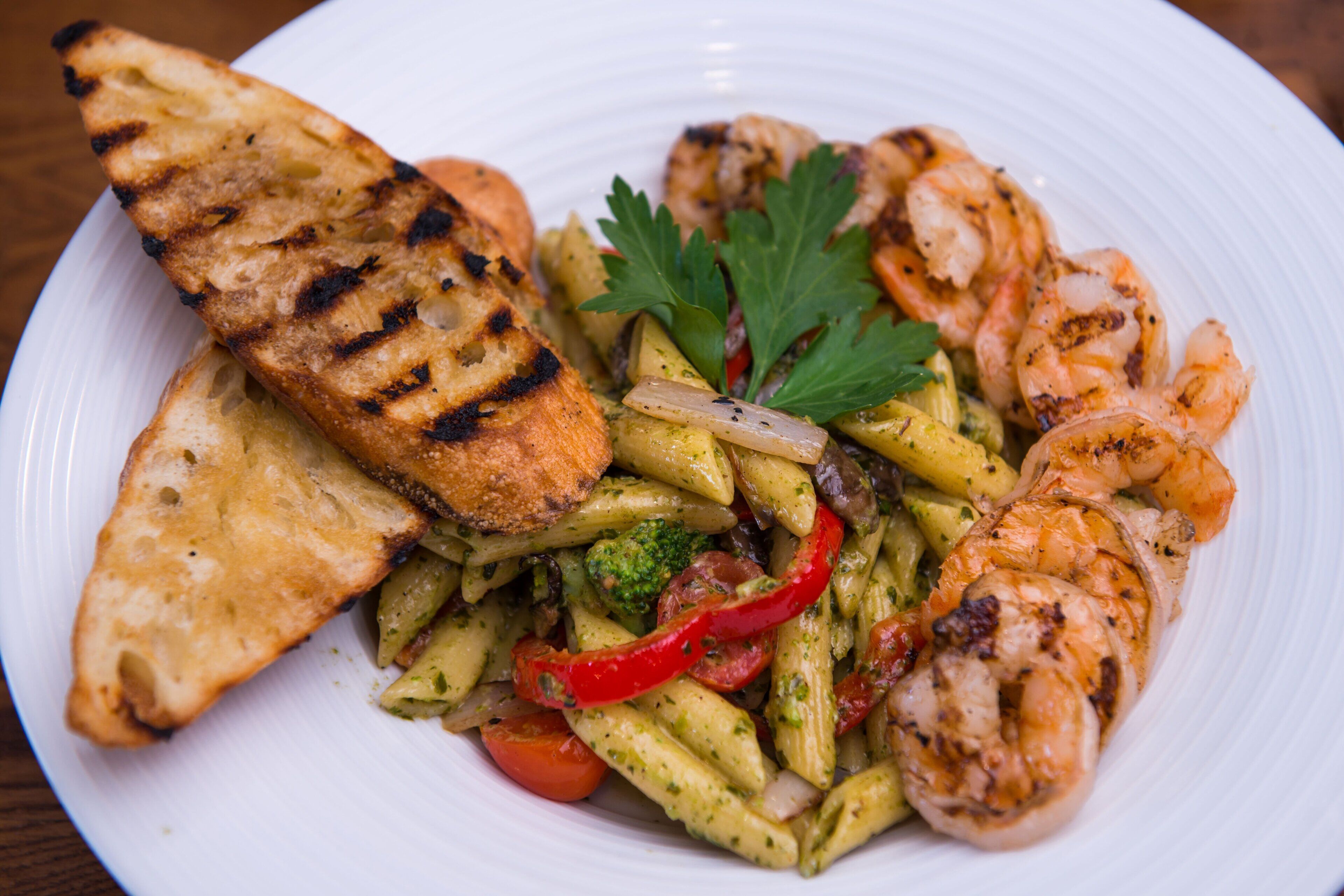 A plate of food with grilled shrimp, grilled bread, and a pasta dish with vegetables.