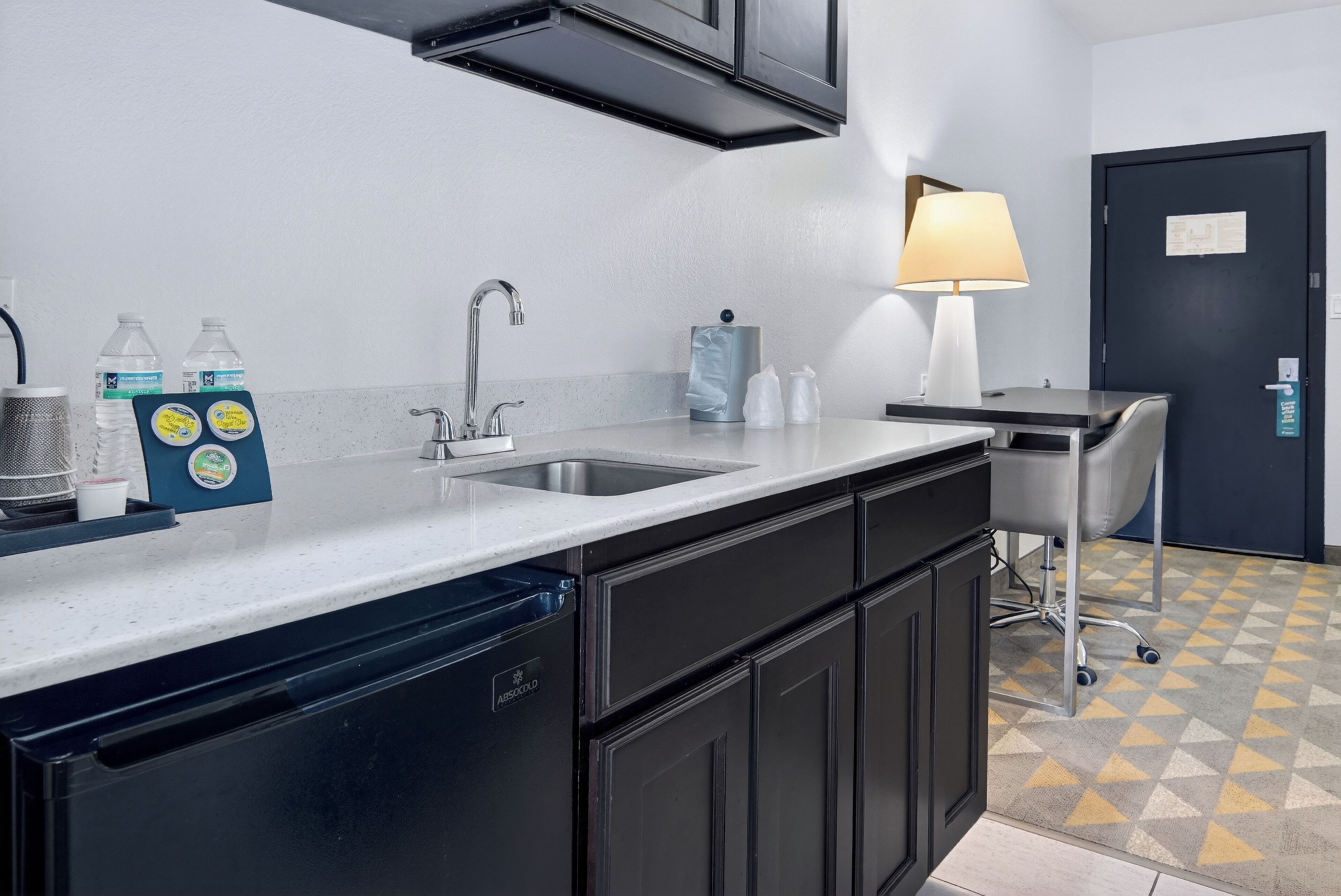 A kitchenette with a sink, a coffee machine, a refrigerator, and a chair.
