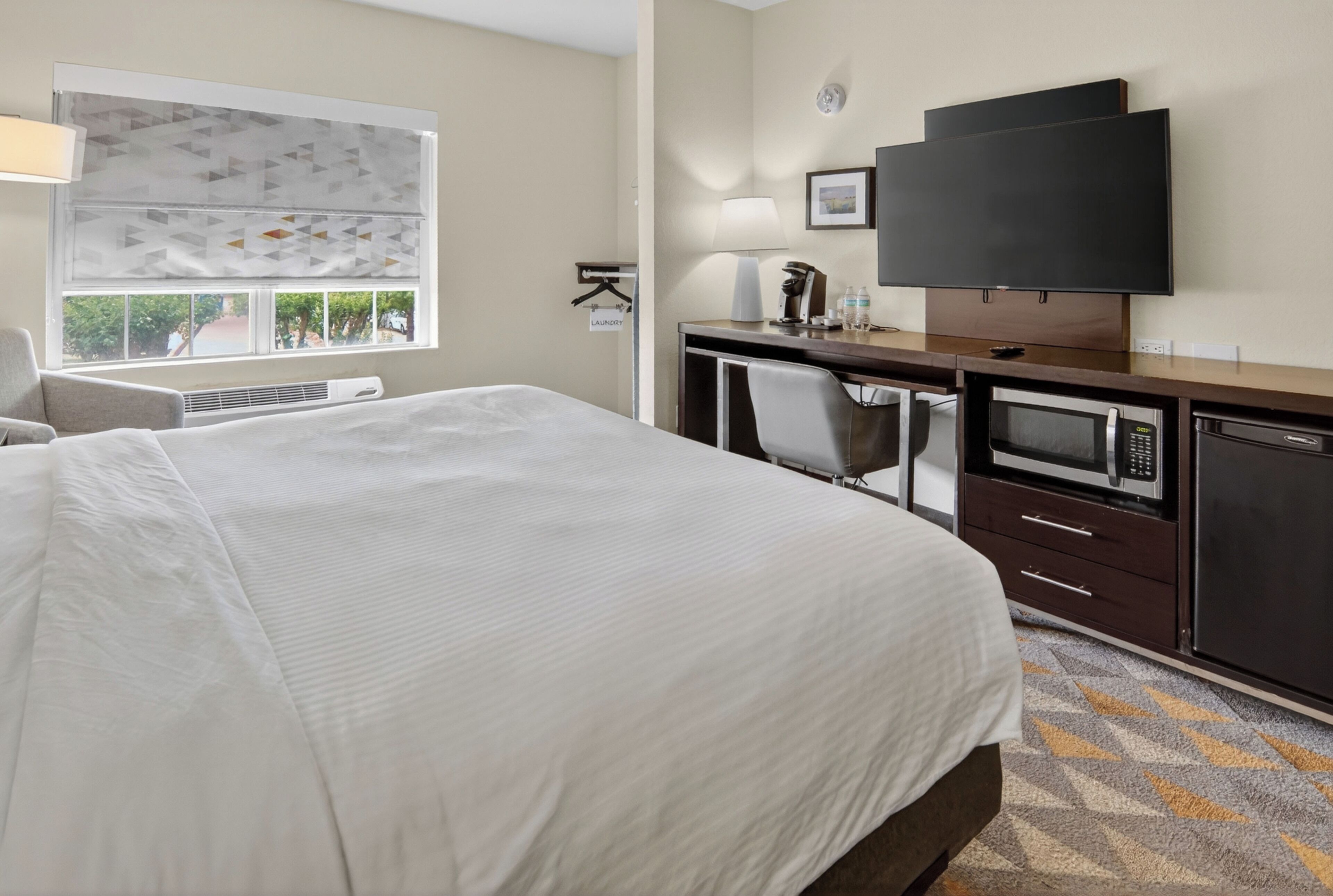 Een hotelkamer met een groot bed, een bureau met een televisie, een magnetron en een kleine kitchenette.