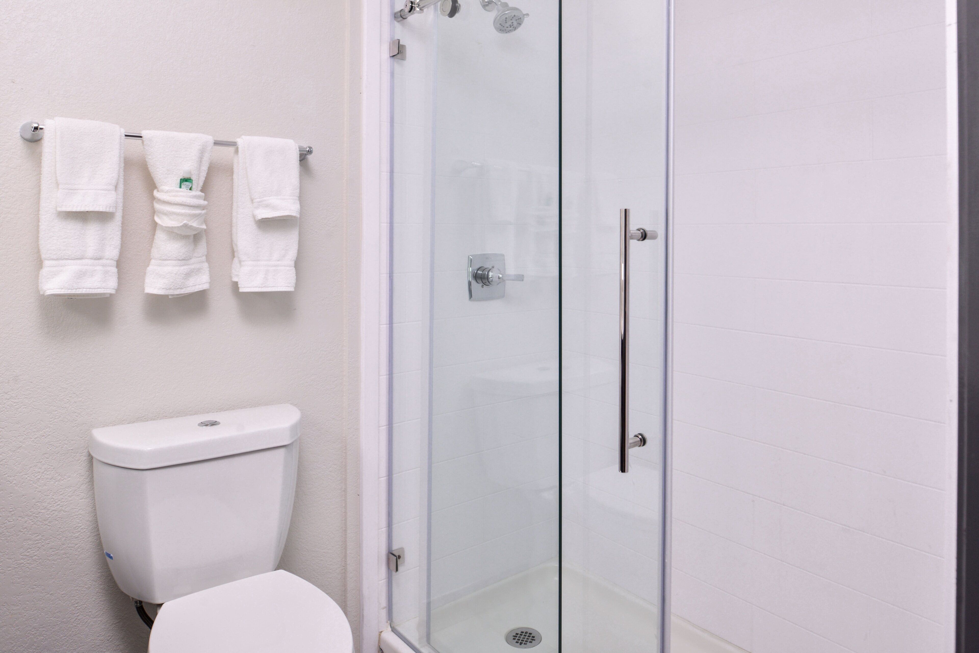 A bathroom with a glass-enclosed shower, a toilet, and a towel rack with multiple towels.