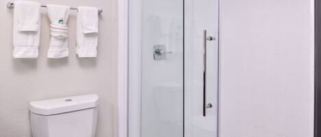 A bathroom with a glass-enclosed shower, a toilet, and a towel rack with multiple towels.