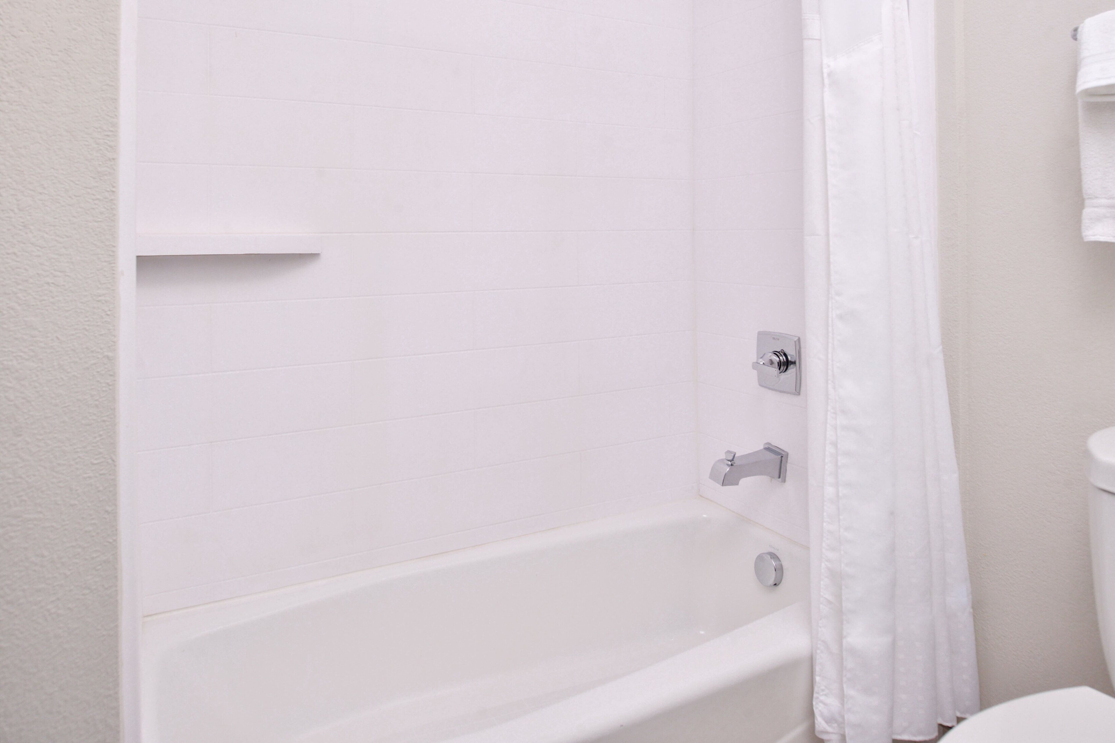 Une baignoire blanche avec un rideau de douche, dans une salle de bain aux murs recouverts de carreaux blancs.
