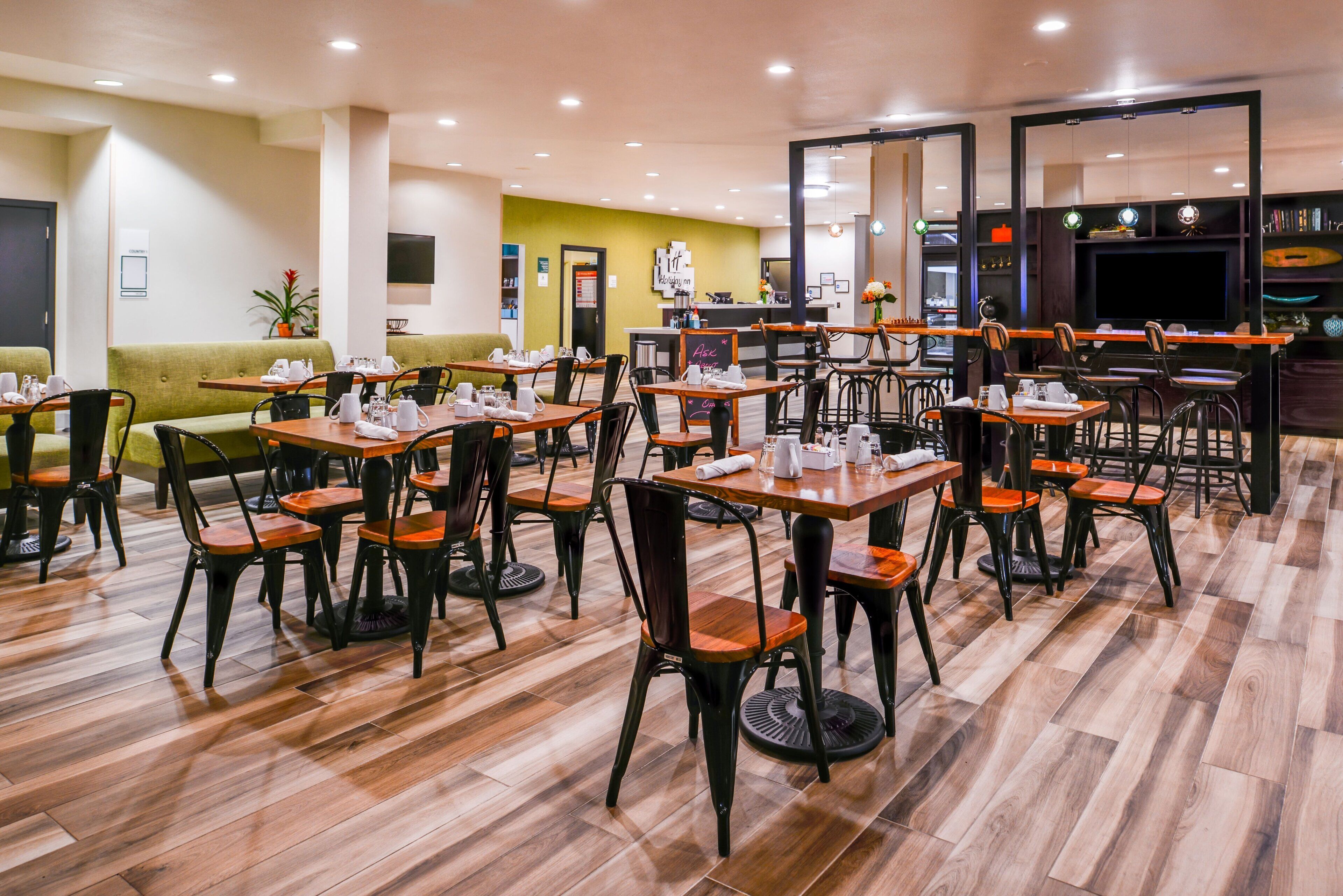 A hotel dining area with multiple tables and chairs, a reception desk, and a green sofa.