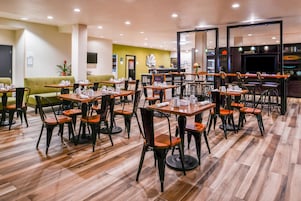 Uma área de refeições de hotel com várias mesas e cadeiras, uma receção e um sofá verde.
