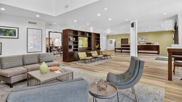 A spacious lobby with a sofa, armchairs, a coffee table, a bookshelf, and a reception desk. - Holiday Inn & Suites Dallas-Addison by IHG (Addison)