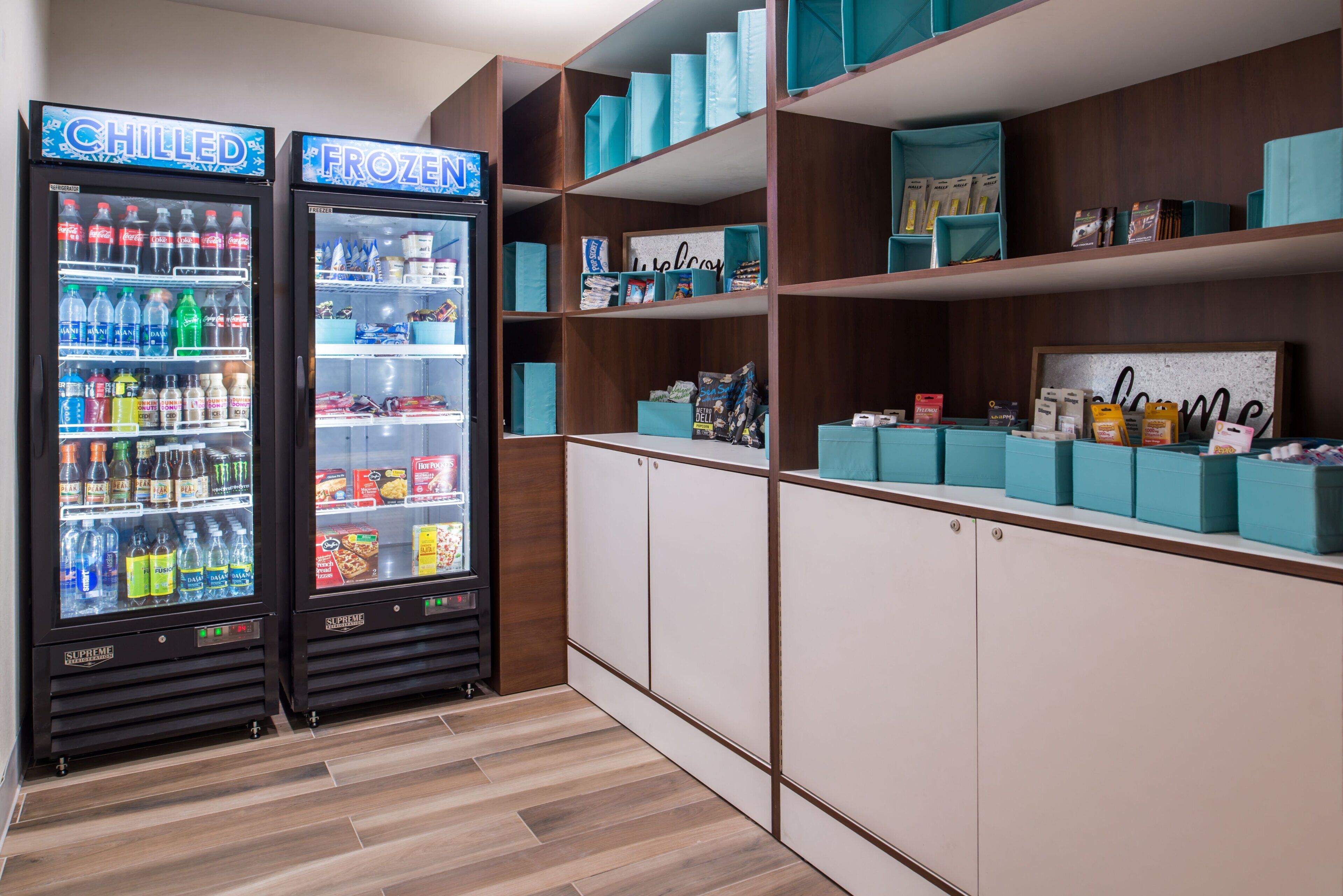 A kitchenette area with two beverage dispensers labeled 'CHILLED' and 'FROZEN,' and shelves stocked with snacks and packaged goods.
