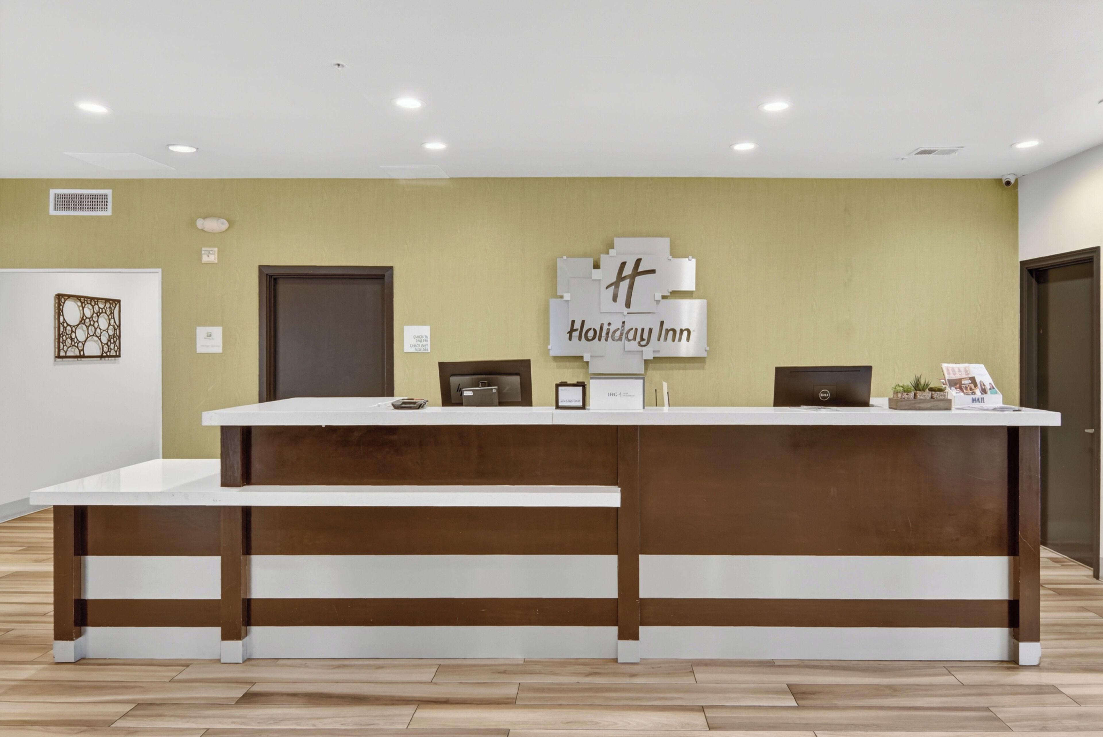 A reception desk with a sign reading 'Holiday Inn,' a computer, a small plant, and a framed picture.