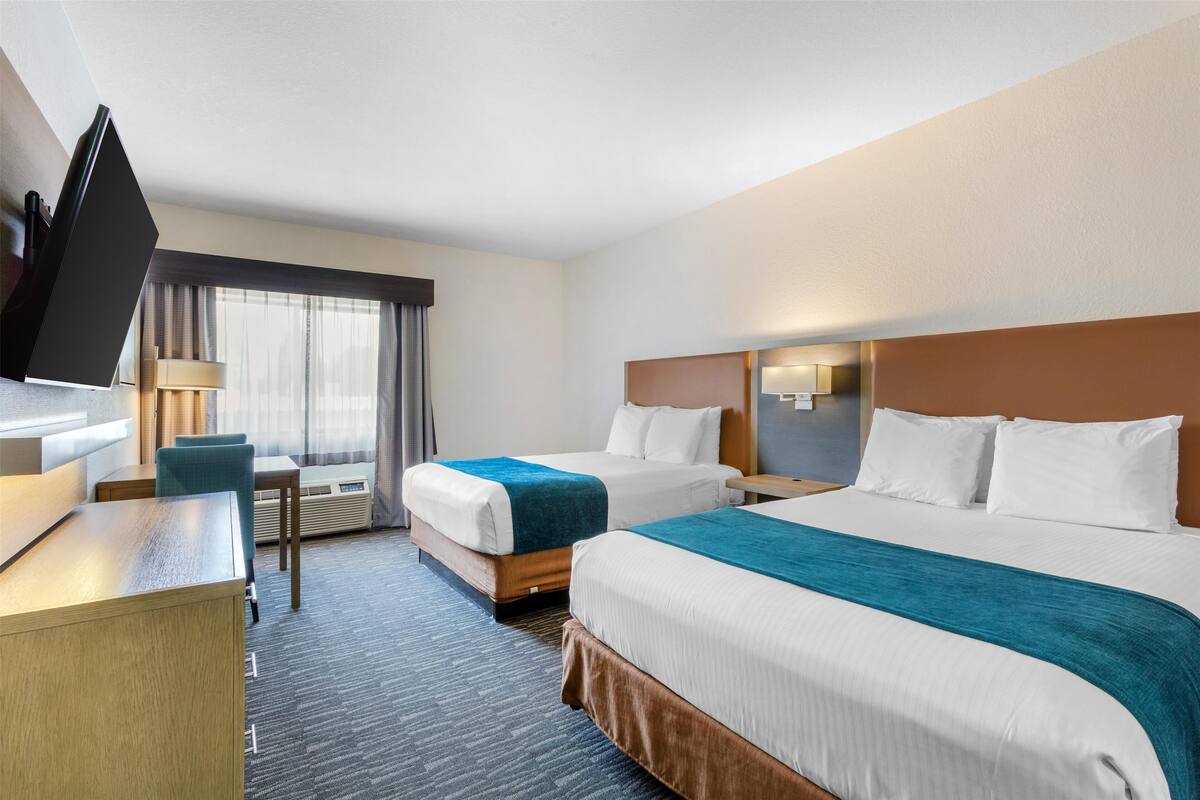 A hotel room with two beds, a desk, a TV, and a window with curtains.
