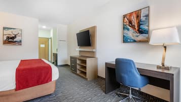 A hotel room with a bed, a desk with a chair, a TV mounted on the wall, and artwork on the walls.