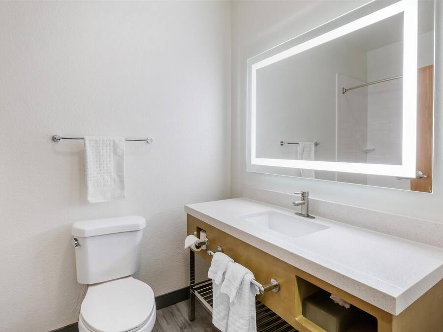 A modern bathroom with a white toilet, a sink with a large mirror, and a towel rack.
