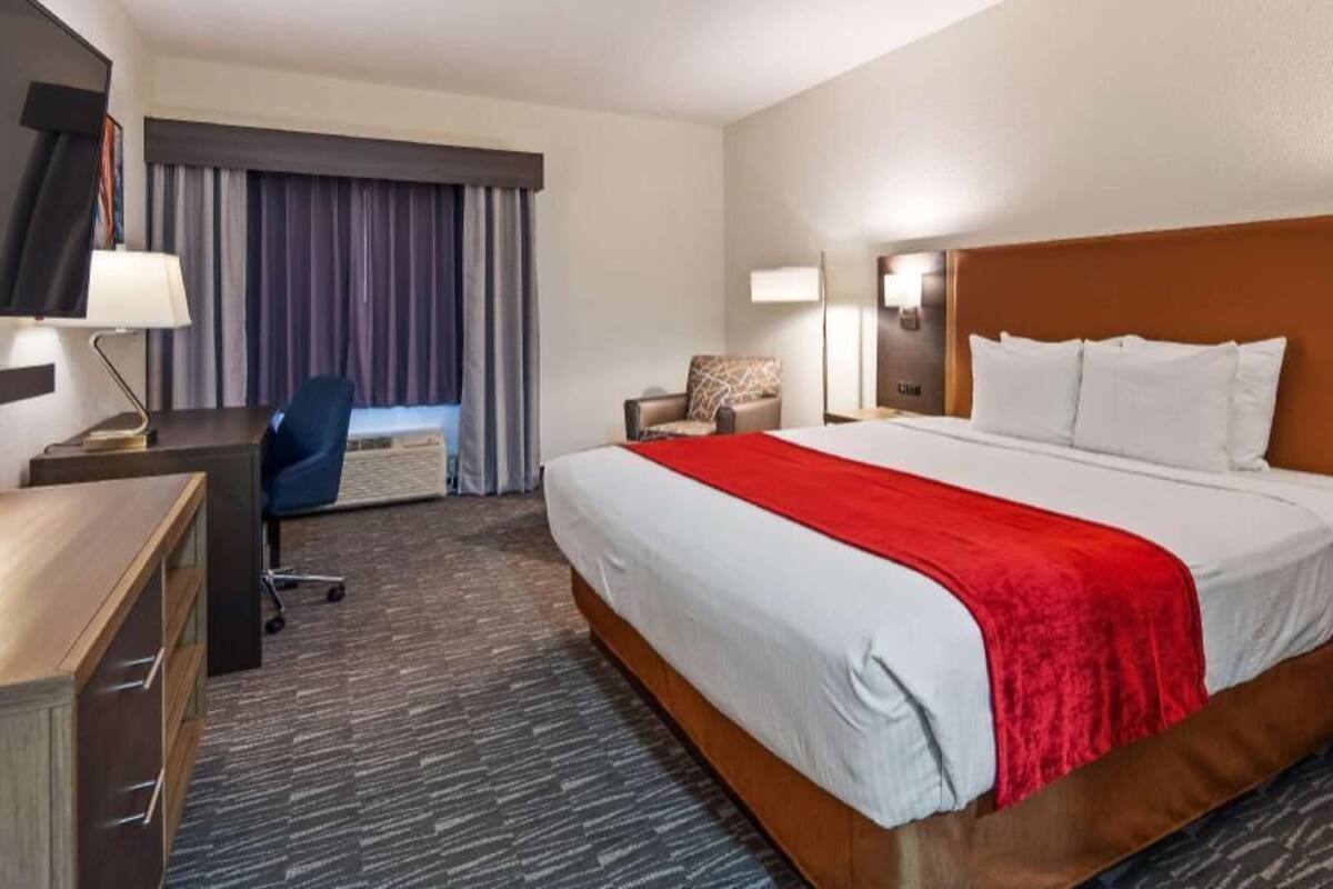 A hotel room with a large bed, a desk, a chair, a TV, and a window with curtains.
