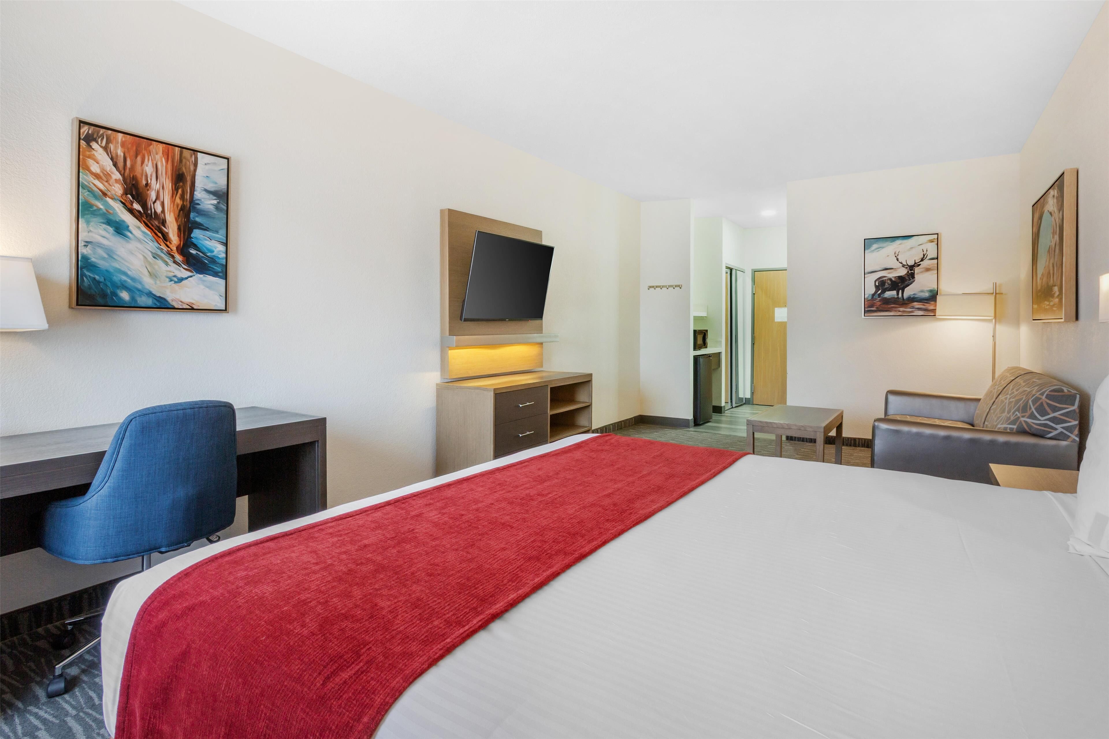 Una habitación de hotel con una cama grande, un escritorio con silla, un televisor y obras de arte en las paredes.