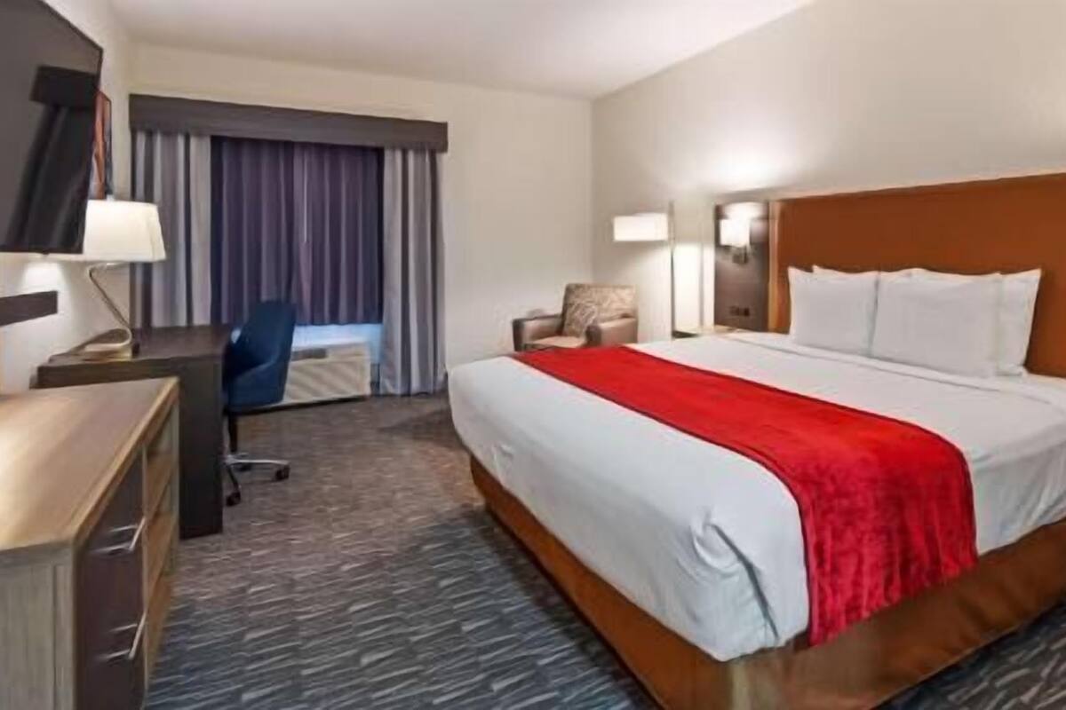 A hotel room with a bed, a desk, a chair, a lamp, and a window with curtains.