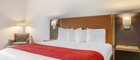 A hotel room with a large bed, a chair, and two wall-mounted lamps.