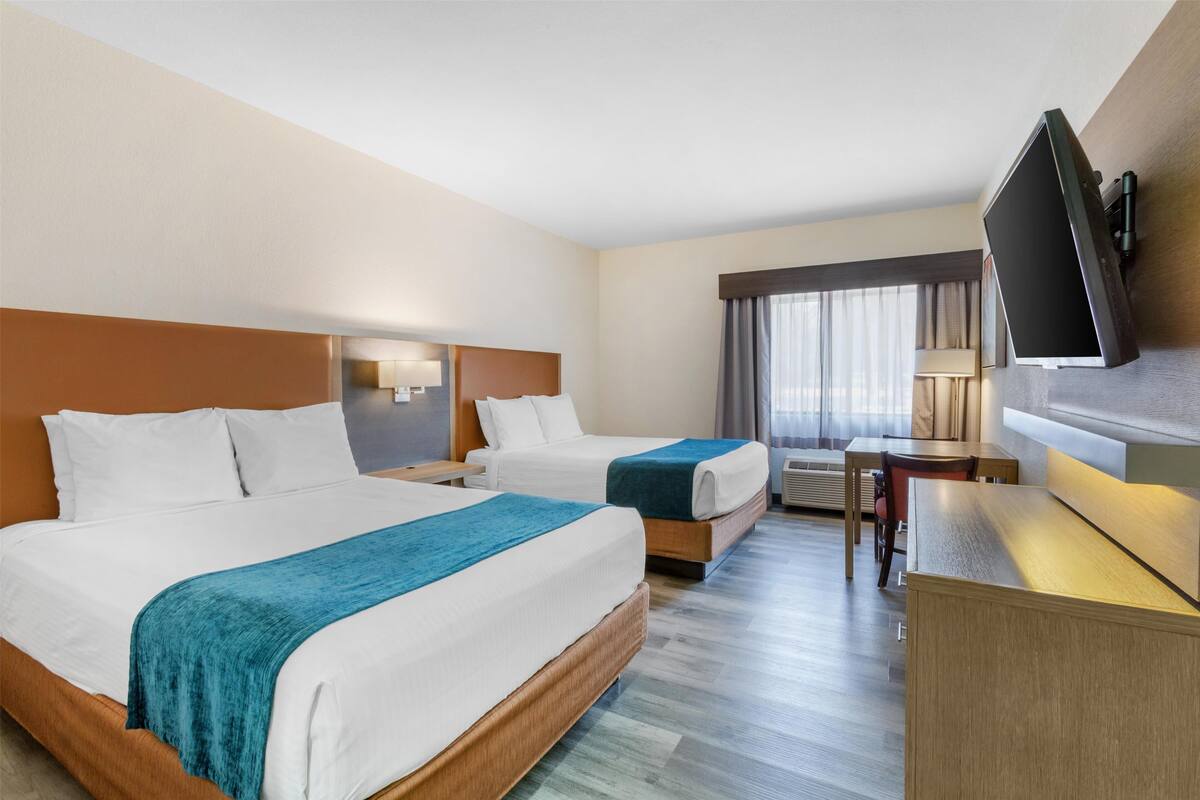 A hotel room with two beds, a desk, a TV, and a window with curtains.