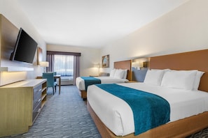 A hotel room with two beds, a desk, a TV, and a window with curtains.