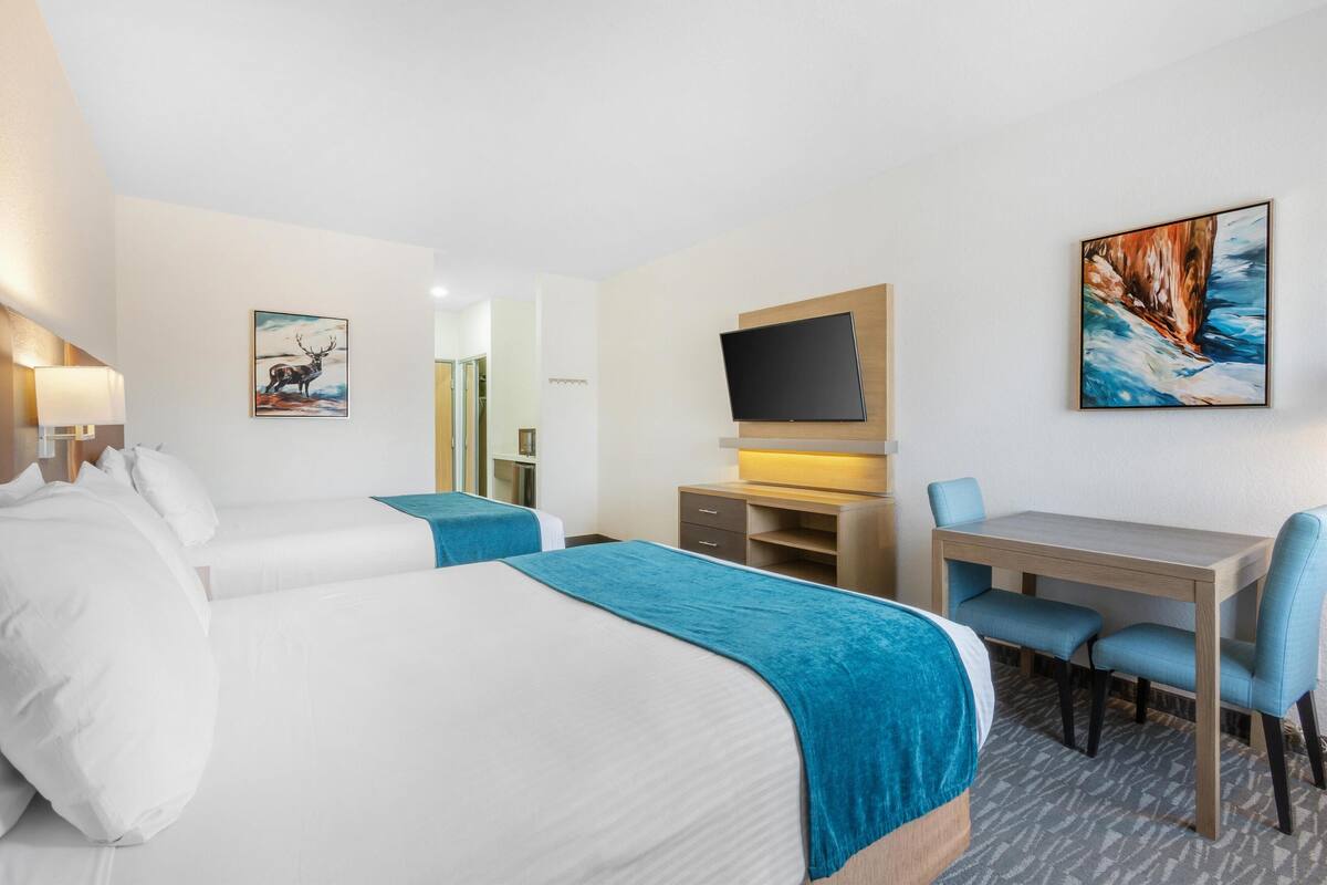 A hotel room with two beds, a desk, a TV, and artwork on the walls.