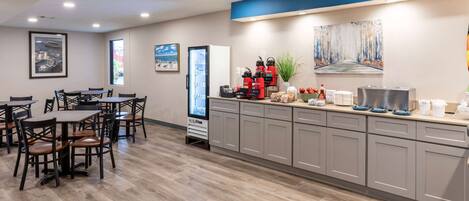 A modern hotel lobby with a dining area, a coffee station, and artwork on the walls.