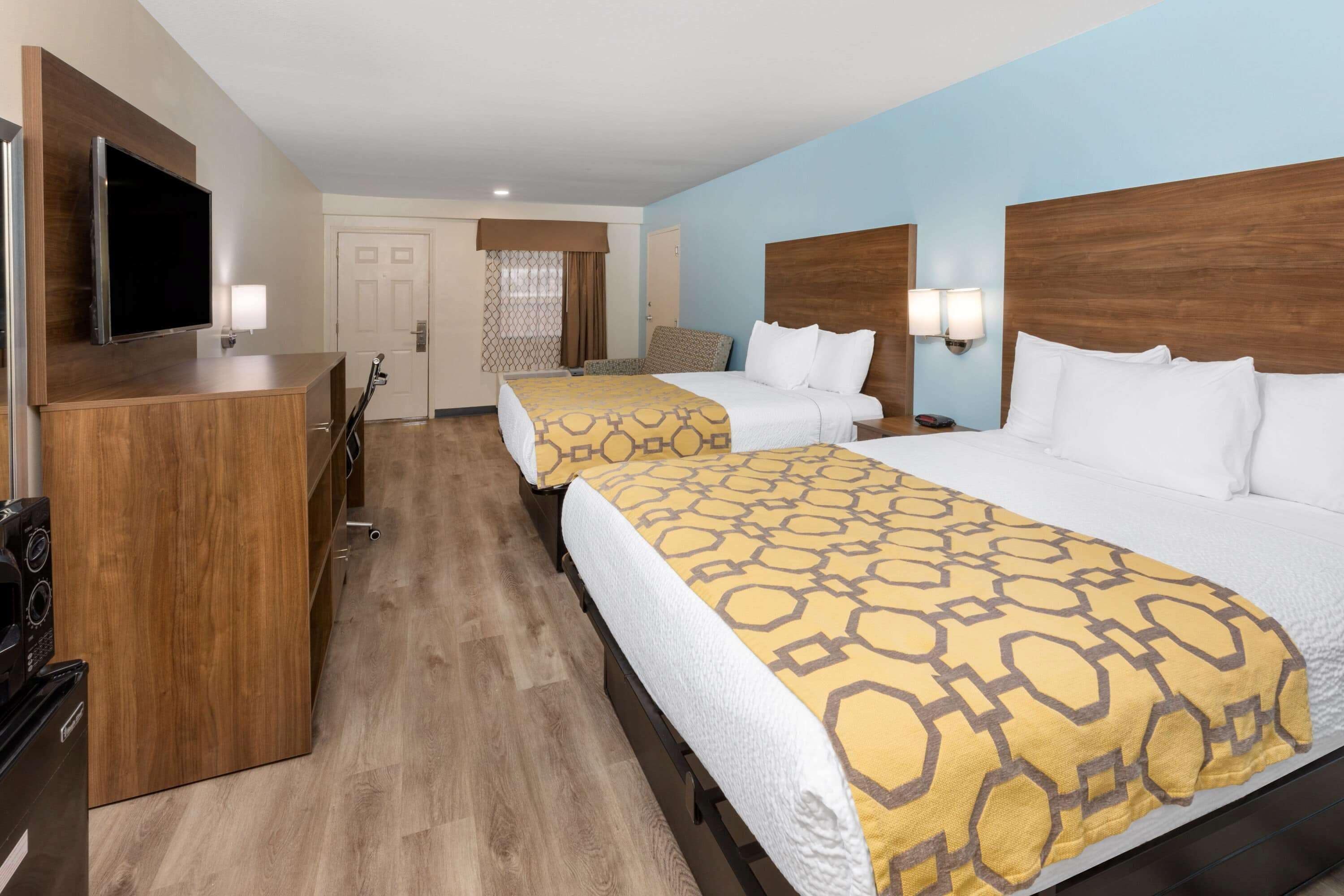 Habitación de hotel con dos camas, televisor, escritorio con ordenador y ventana con cortinas.