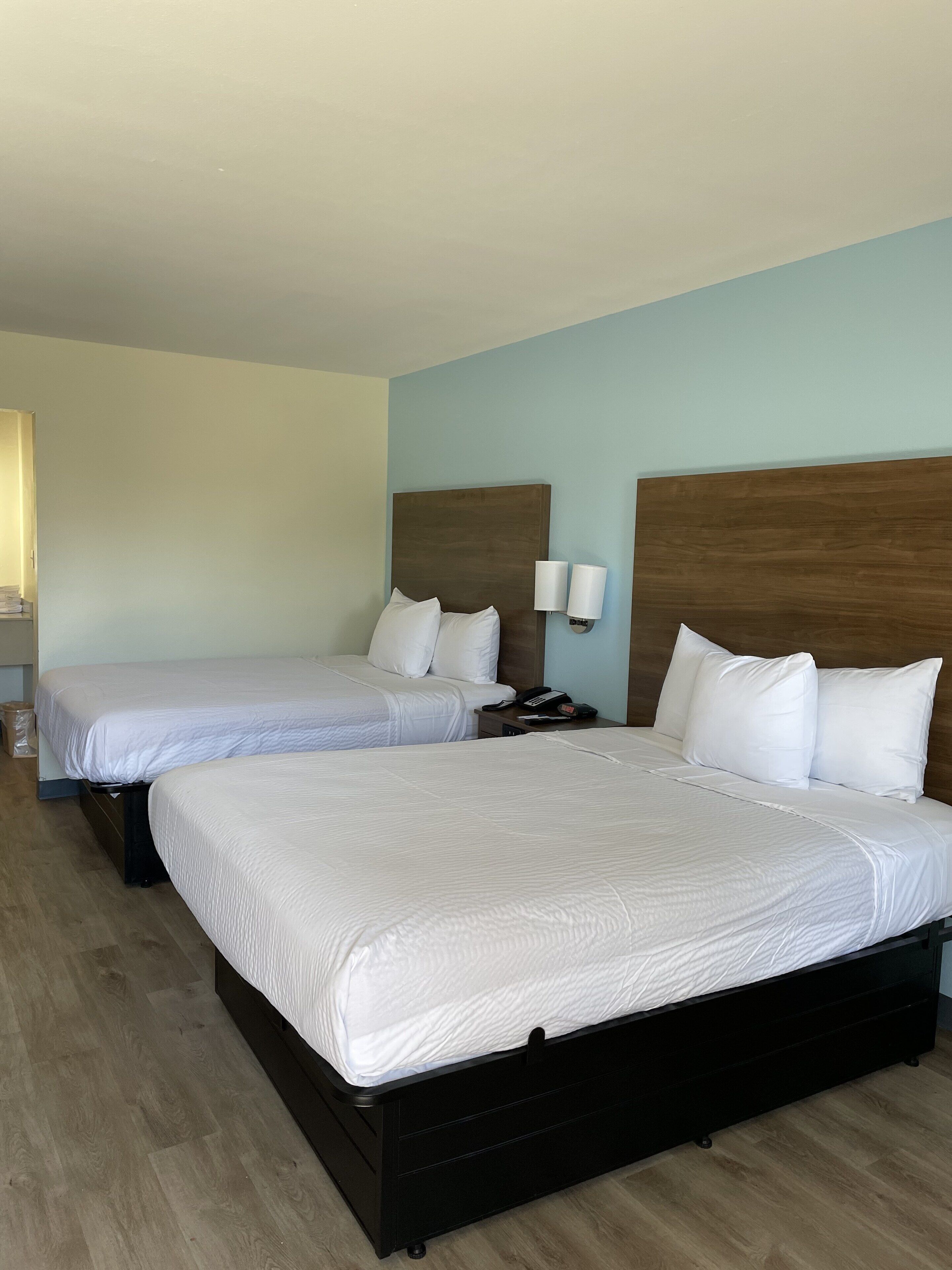 Habitación de hotel con dos camas, cabeceros de madera, ropa de cama blanca y una mesita de noche con teléfono.