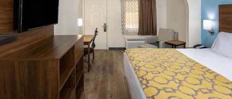 Una habitación de hotel con una cama grande, un televisor montado en un aparador de madera, un escritorio con una silla y un equipo de aire acondicionado.