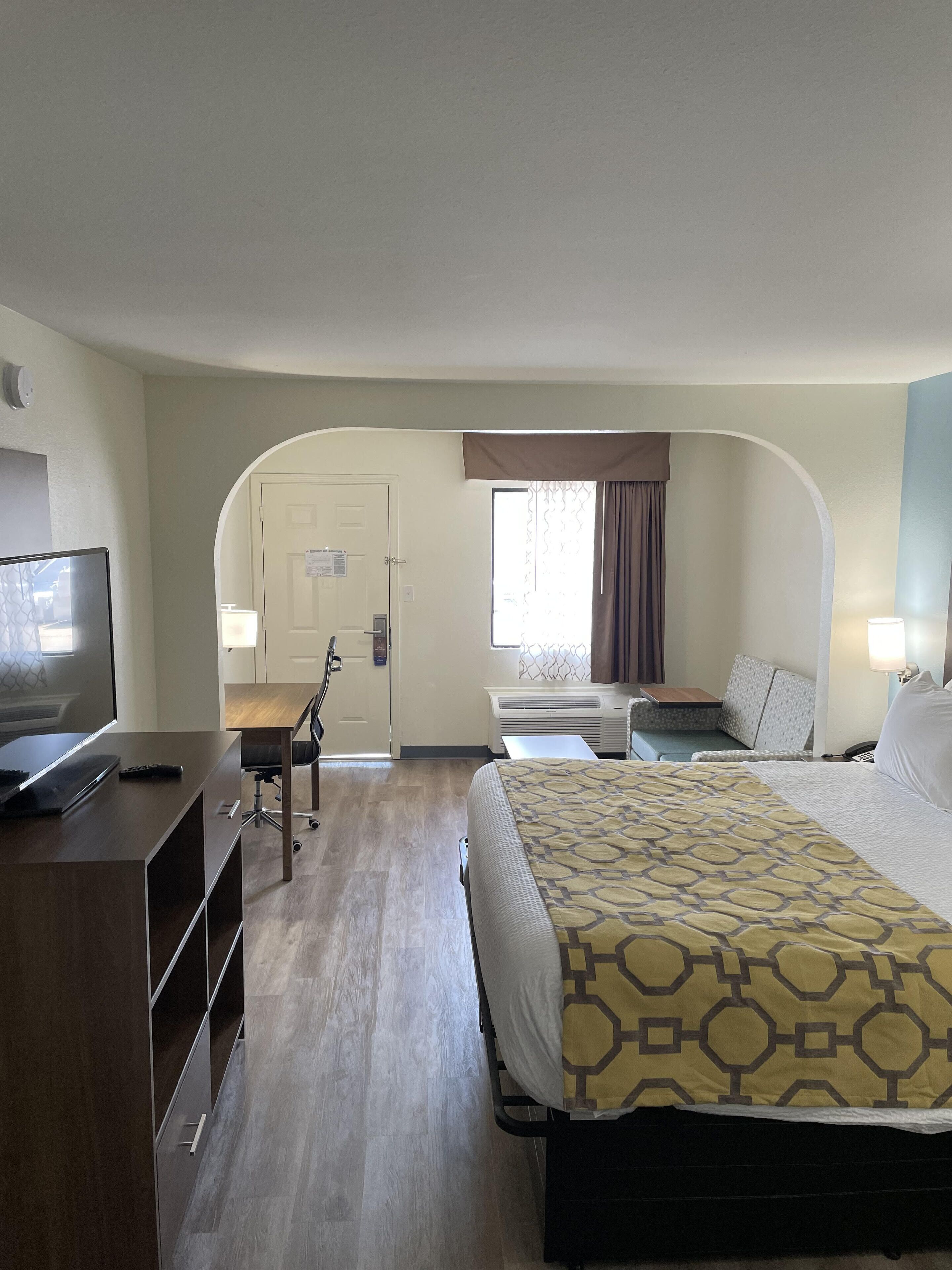 A hotel room with a bed, a desk, a chair, a TV, and a window with curtains.