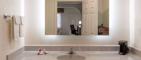 A bathroom with a large mirror, a sink, a coffee maker, and a towel rack.