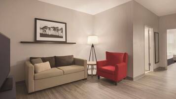 Un salon moderne avec un canapé beige, un fauteuil rouge, une lampe sur pied et un tableau encadré accroché au mur.