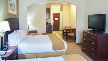 Una habitación de hotel con cama, escritorio con lámpara, televisión y zona de comedor con mesa y sillas.