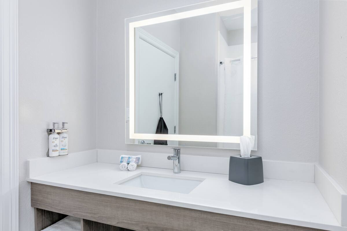A modern bathroom with a white sink, a large mirror, and a towel dispenser.