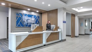 A modern reception desk with a blue geometric wall design, a wooden accent, and a sign indicating the E-Press Shop. - Holiday Inn Express Hotel & Suites Winnie by IHG (Winnie)