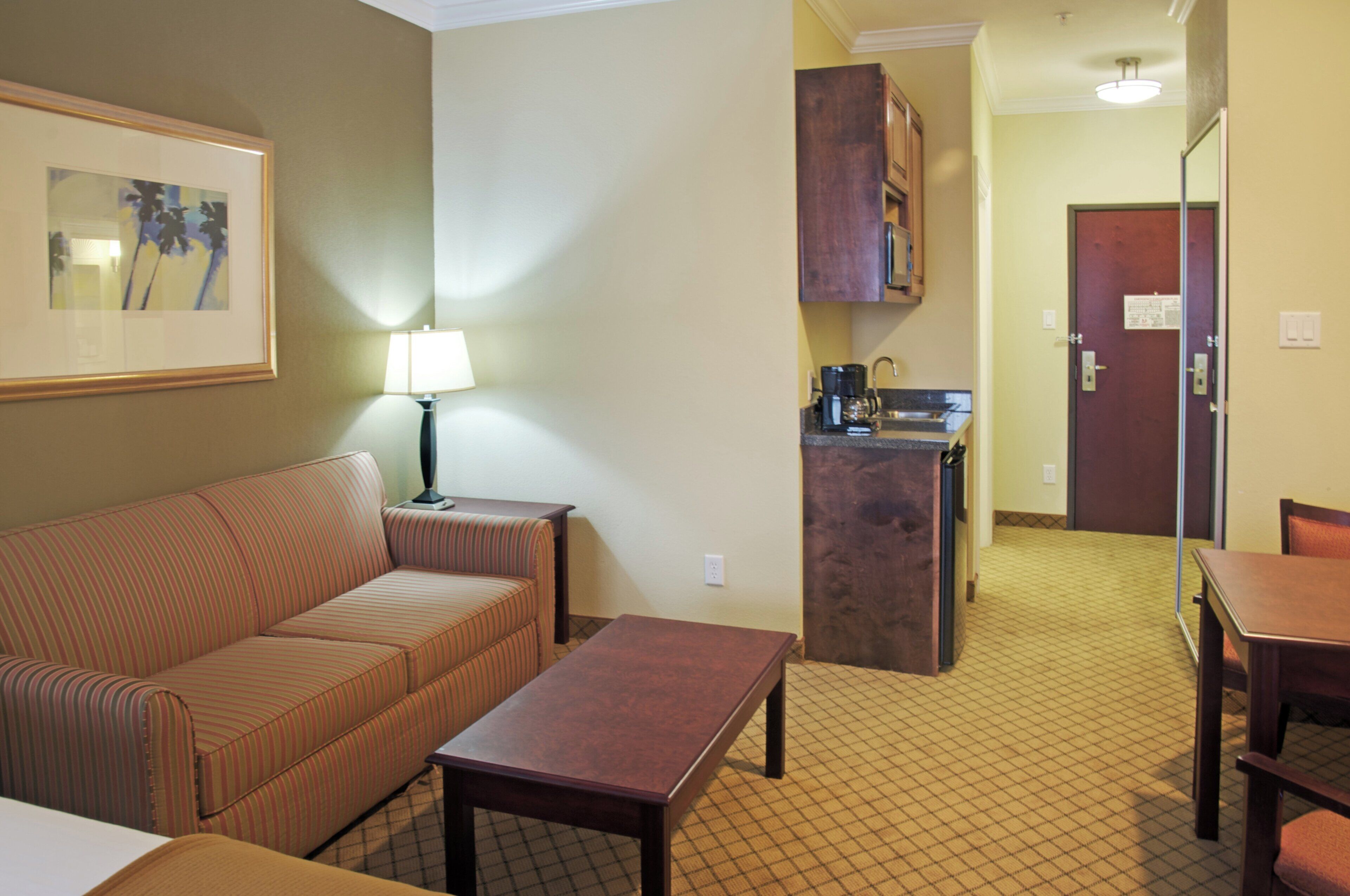 Une chambre d’hôtel avec un canapé, une table, une lampe, un coin cuisine et une porte.