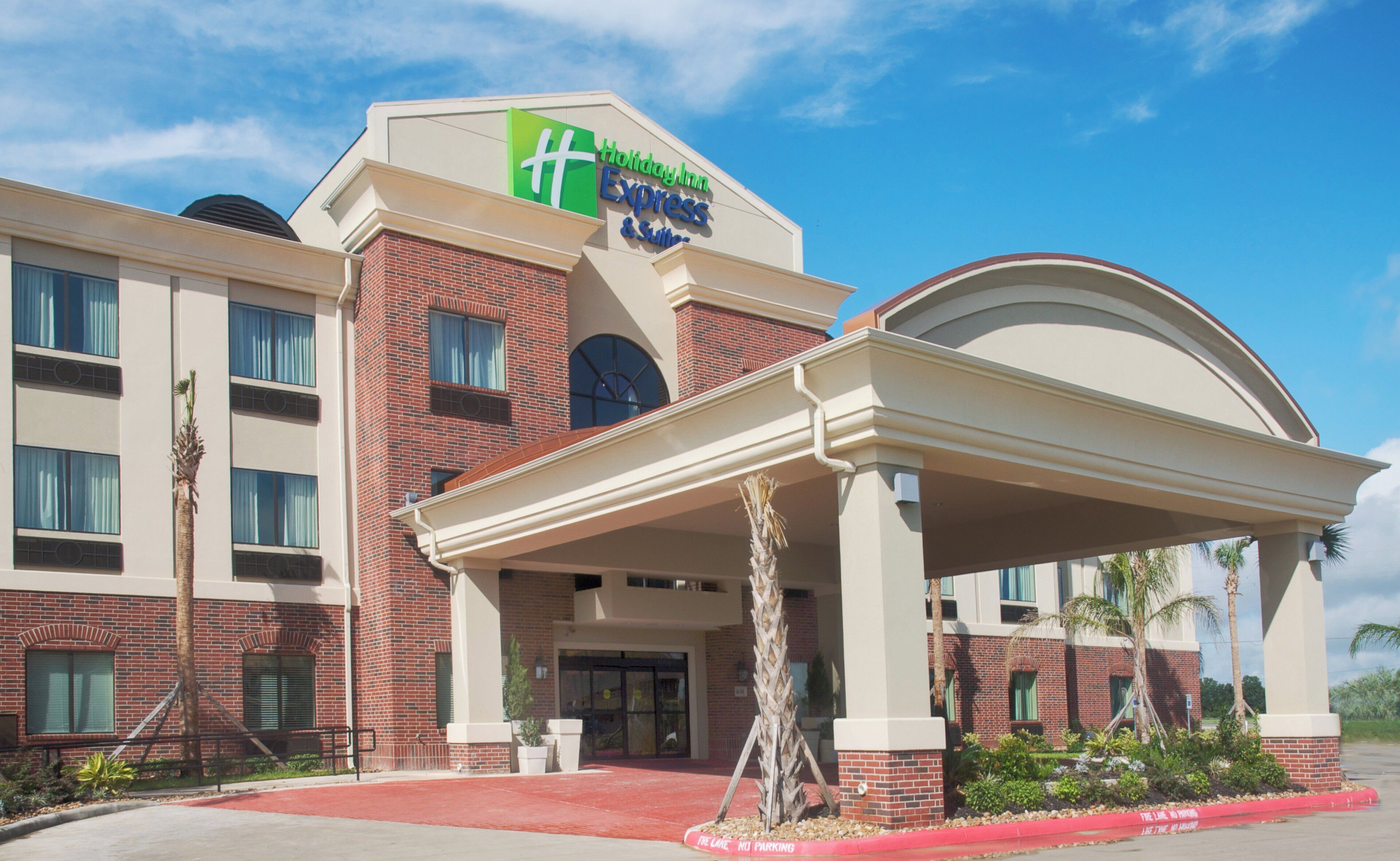A Holiday Inn Express & Suites hotel with a brick facade, a covered entrance, and a red curb indicating no parking.