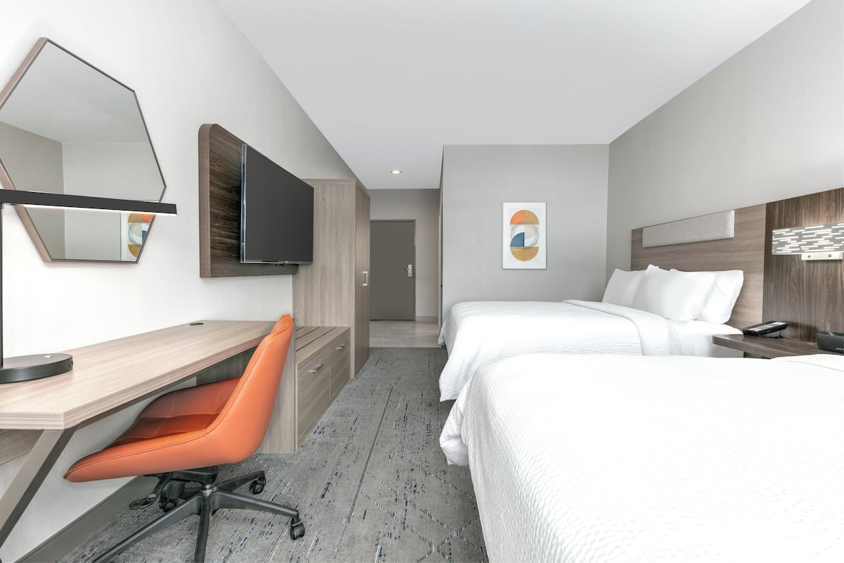 Una habitación de hotel moderna con escritorio, dos camas, una silla y televisión.