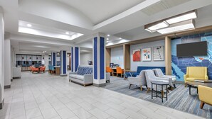 A spacious lobby with a modern design, featuring a central seating area with sofas and armchairs, a dining area with orange chairs, and a large wall-mounted TV. - Holiday Inn Express Hotel & Suites Winnie by IHG (Winnie)
