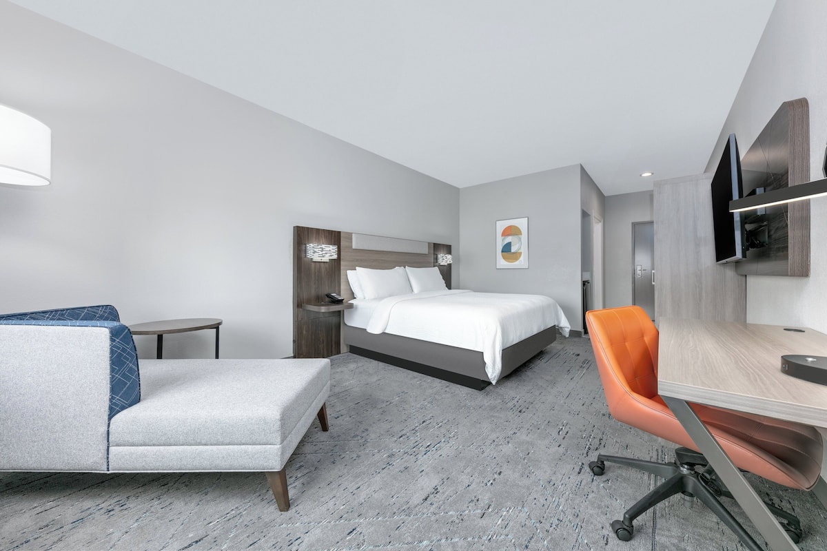 Una habitación de hotel moderna con una cama, un escritorio, una silla y una mesita.