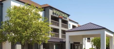 A Courtyard by Marriott hotel with a covered entrance, a tree in front, and a clear sky.