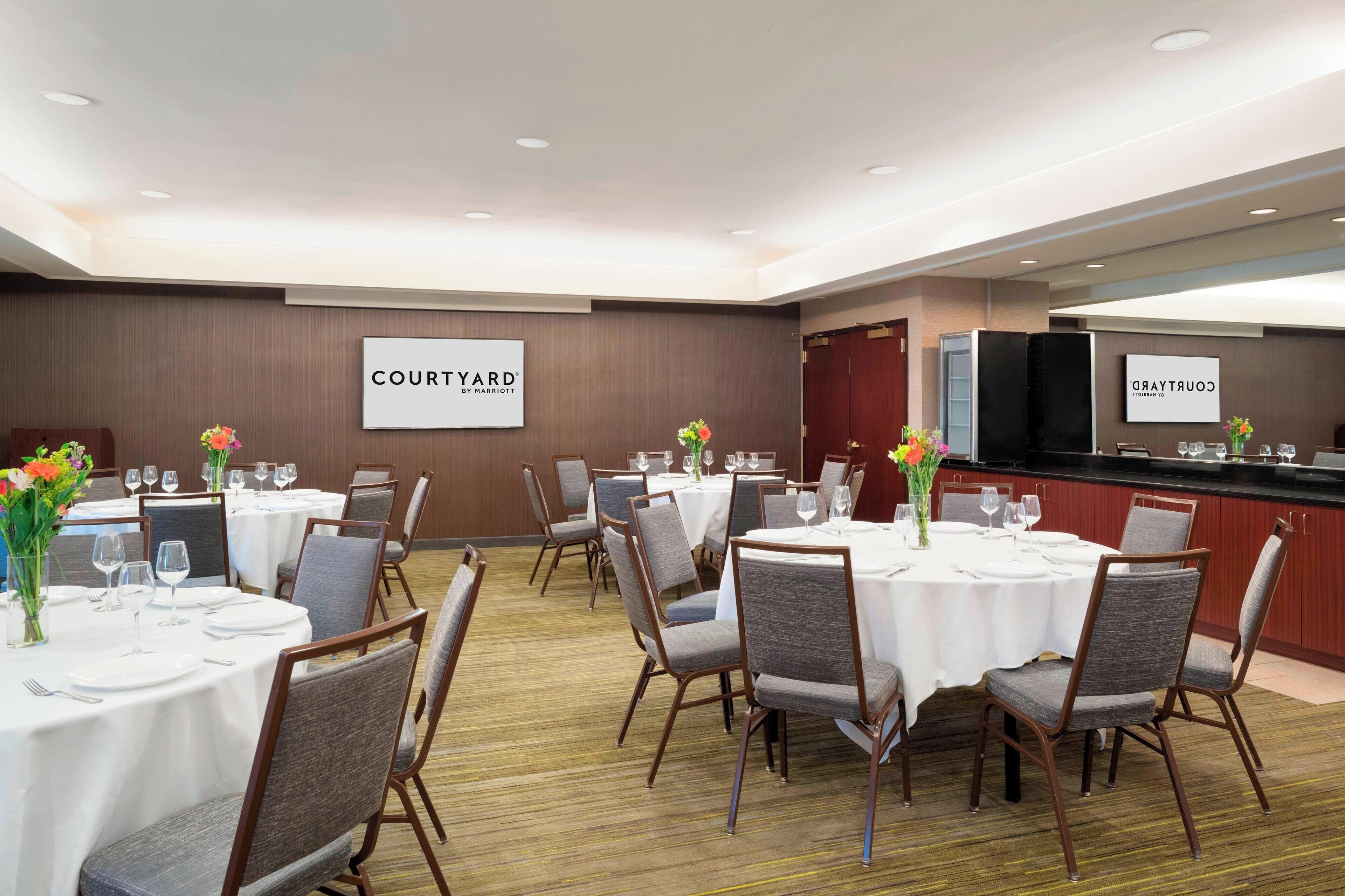 A hotel conference room with multiple tables, chairs, and a counter with a television.