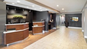 A modern reception area with wooden reception desks, a flat-screen TV, and a potted plant. - Courtyard by Marriott Princeton (Princeton)