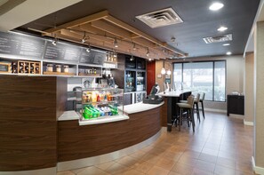A modern bar area with a curved wooden counter, a menu board, and a seating area with a table and chairs. - Courtyard by Marriott Princeton (Princeton)