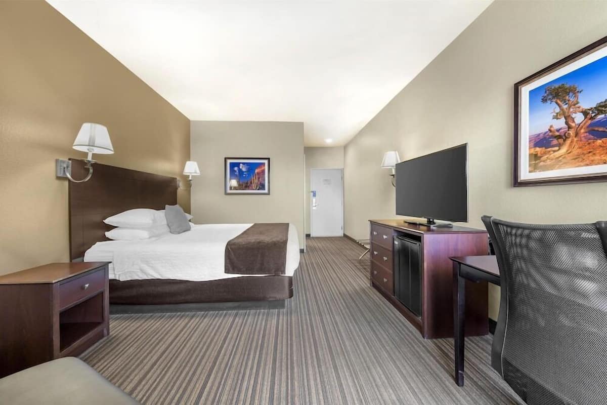 A hotel room with a bed, desk, TV, and artwork on the walls.